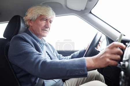 Foto de Retrato de vista lateral del hombre mayor de pelo blanco usando la radio mientras conduce en el coche, espacio de copia - Imagen libre de derechos
