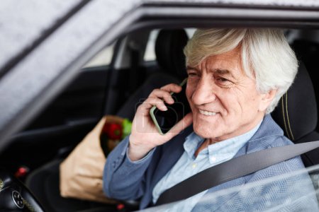 Portrait of smiling senior man speaking by phone and driving car, copy space