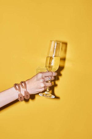 Photo for Pop color closeup of female hand holding tall champagne glass in celebration against minimal yellow background, copy space - Royalty Free Image