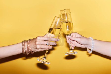 Photo for Vibrant close up image of two people clinking champagne glasses on yellow background in celebration - Royalty Free Image