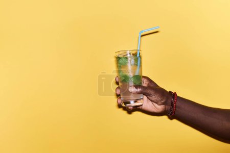 Téléchargez les photos : Minimal close up of male hand holding refreshing ice cocktail against vibrant yellow background, copy space - en image libre de droit