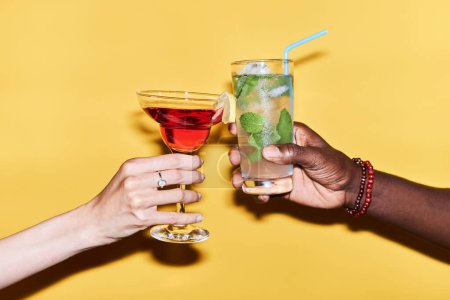 Téléchargez les photos : Minimal close up of multiethnie couple clinking cocktails sur fond jaune vif - en image libre de droit