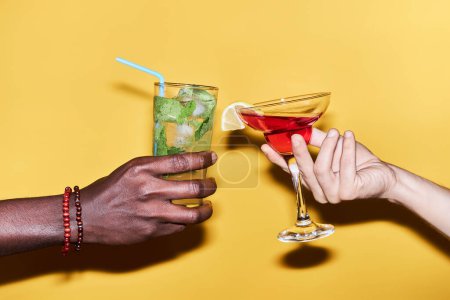 Photo for Close up of multiethnic young couple holding two cocktails against vibrant yellow background - Royalty Free Image