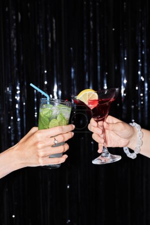 Photo for Vertical closeup of two people clinking cocktail glasses against glittering party background, copy space - Royalty Free Image