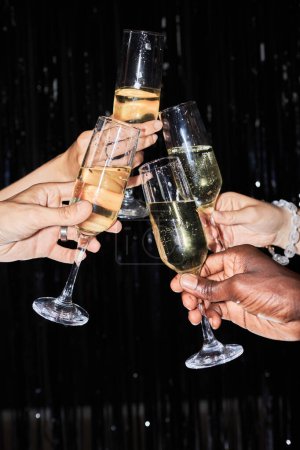Photo for Closeup of hands holding champagne glasses against glittering background and toasting at party - Royalty Free Image