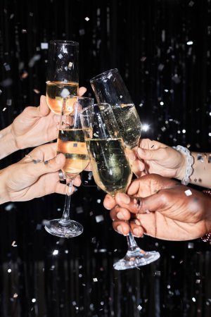 Photo for Closeup of group of friends toasting with champagne glasses at party against glittering background with confetti - Royalty Free Image