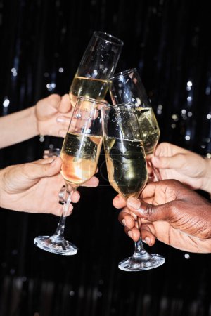 Foto de Primer plano vertical de amigos sosteniendo copas de champán en la fiesta contra el fondo brillante - Imagen libre de derechos