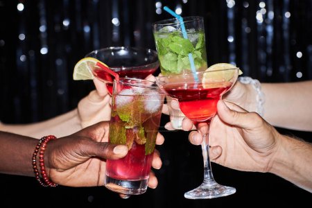 Photo for Close up of group of friends holding cocktails and toasting against glittering party background, copy space - Royalty Free Image