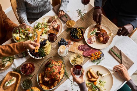 Foto de Vista de alto ángulo en diversos grupos de amigos disfrutando de comida casera en la mesa de cena festiva con pavo asado o pollo, espacio para copiar - Imagen libre de derechos