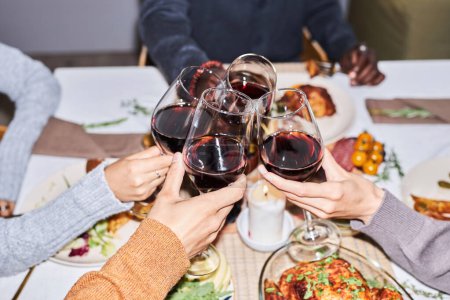 Foto de Primer plano del grupo de amigos brindando con copas de vino tinto en la mesa de la cena, filmado con flash - Imagen libre de derechos