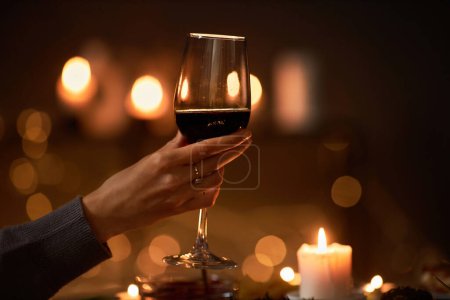 Foto de Primer plano de la mano femenina sosteniendo copa de vino en la mesa con luces de Navidad en el fondo, espacio de copia - Imagen libre de derechos
