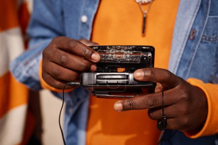Photo for Close-up of young African American man in casualwear putting cassette into old walkman with earphones while standing in front of camera - Royalty Free Image