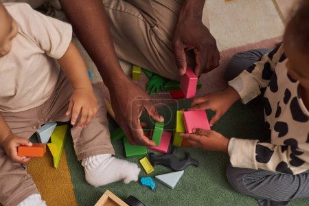 Photo for Top view closeup of Black father with two children sitting on floor at home and playing with wooden toys together, copy space - Royalty Free Image