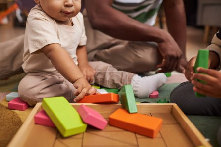 Foto de Primer plano de bebé lindo jugando con ladrillos de juguete de madera en el suelo en casa con la familia, espacio de copia - Imagen libre de derechos