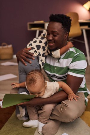 Photo for Vertical portrait of young Black man babysitting two wiggly little kids struggling to parent - Royalty Free Image