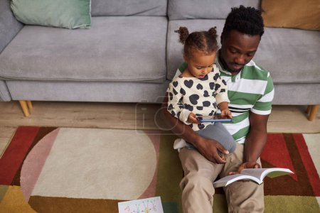 Foto de Vista superior en el padre joven negro con la niña pequeña sentada en el suelo en casa juntos y utilizando el teléfono inteligente, espacio de copia - Imagen libre de derechos