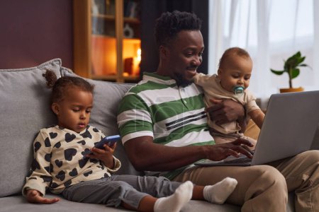 Portrait de jeune père au travail avec deux enfants utilisant un ordinateur portable et souriant appréciant la parentalité, espace de copie