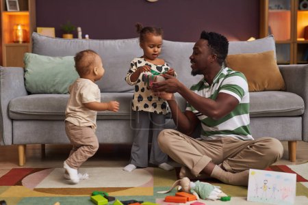 Téléchargez les photos : Portrait complet de père noir heureux présentant un cadeau à la petite fille mignonne à la maison, espace de copie - en image libre de droit