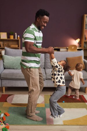 Foto de Retrato vertical de cuerpo entero de feliz padre negro bailando con una linda niña en casa en la sala de estar - Imagen libre de derechos