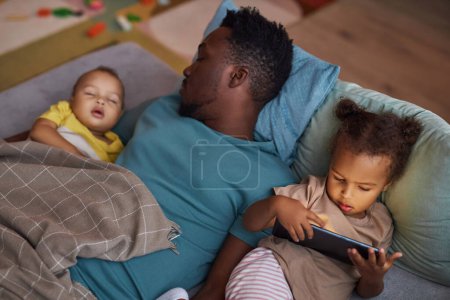 Photo for Portrait of little Black girl using smartphone with sleeping father at naptime - Royalty Free Image