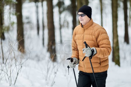 Active senior man wear sunglasses when trekking in forest on winter