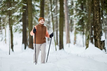 Excited active senior woman trekking in beautiful winter forest, enjoy views and fresh air