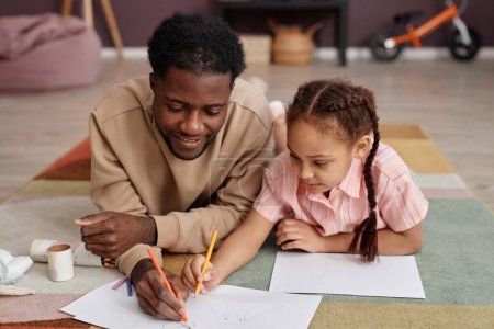 Photo for Portrait of Black father and daughter drawing pictures together laying on floor at home and smiling - Royalty Free Image