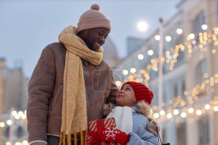 Téléchargez les photos : Portrait taille haute de la famille afro-américaine heureuse., père et fille se regardant à l'extérieur en hiver et tenant cadeau de Noël - en image libre de droit