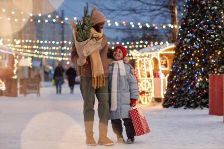 Foto de Retrato de larga duración de feliz familia negra padre e hija disfrutando de las compras de Navidad al aire libre en invierno y sonriendo alegremente - Imagen libre de derechos