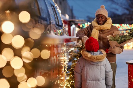 Téléchargez les photos : Portrait de heureux père et fille noirs achetant des collations au camion alimentaire dans le marché de Noël, espace de copie - en image libre de droit