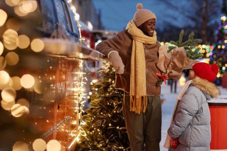 Téléchargez les photos : Portrait de famille afro-américaine heureuse avec père et fille profitant du shopping au marché de Noël en hiver - en image libre de droit
