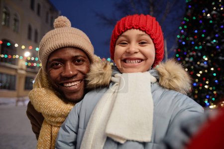 Foto de POV de feliz padre negro e hija tomando foto selfie al aire libre juntos en invierno y mirando a la cámara - Imagen libre de derechos