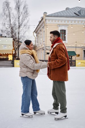 Téléchargez les photos : Portrait complet de jeune couple patinant ensemble et se tenant la main en appréciant la date d'hiver amusante à l'extérieur - en image libre de droit