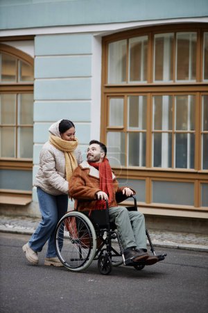 Téléchargez les photos : Portrait vertical d'une jeune femme aidant un homme handicapé tout en profitant du temps passé ensemble en ville - en image libre de droit