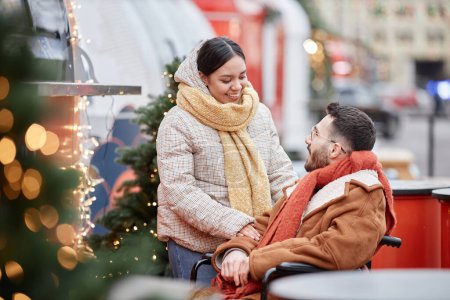Foto de Retrato de mujer joven sonriendo a su pareja con discapacidad mientras se divierten al aire libre en el mercado de Navidad - Imagen libre de derechos