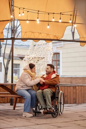 Foto de Retrato vertical de larga duración de pareja joven con discapacidad disfrutando de una cita al aire libre con luces de Navidad - Imagen libre de derechos