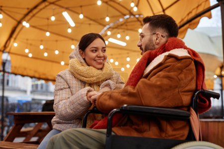 Foto de Retrato de una joven sonriente hablando con un hombre con discapacidad disfrutando de una cita al aire libre en invierno, espacio para copiar - Imagen libre de derechos