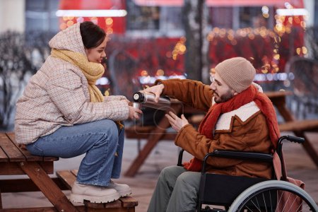 Foto de Retrato de hombre con discapacidad compartiendo bebidas calientes con una mujer joven disfrutando de una cita en la ciudad de invierno - Imagen libre de derechos