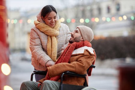 Foto de Retrato de feliz pareja joven con el hombre usando silla de ruedas disfrutando de la fecha al aire libre en la ciudad de invierno - Imagen libre de derechos