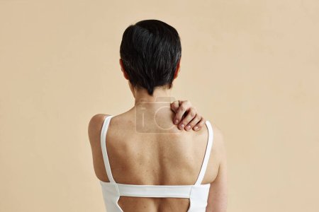 Adult woman hiding standing with bare back against minimal beige background, copy space