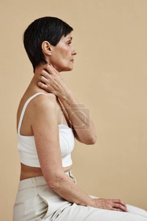 Minimal side view of adult woman scratching neck against neutral background