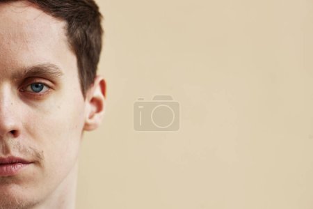 Foto de Mitad retrato de hombre joven con ojos azules llamativos sobre fondo neutro, espacio de copia - Imagen libre de derechos