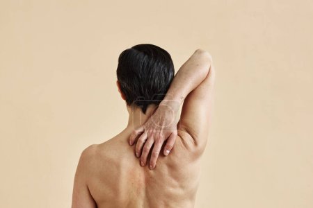 Téléchargez les photos : Vue arrière minimale de la femme adulte se gratter dos nu sur fond beige, espace de copie - en image libre de droit