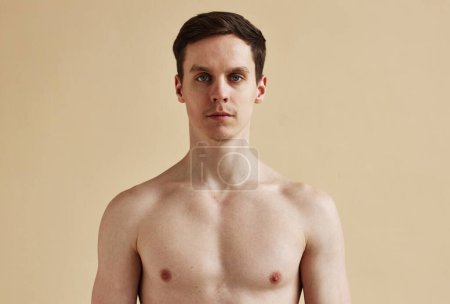 Foto de Retrato mínimo de un joven sin camisa mirando a la cámara con ojos azules sobre un fondo pálido, espacio para copiar - Imagen libre de derechos