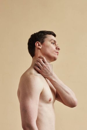 Foto de Vertical side view of young man scratching itchy skin, minimal - Imagen libre de derechos