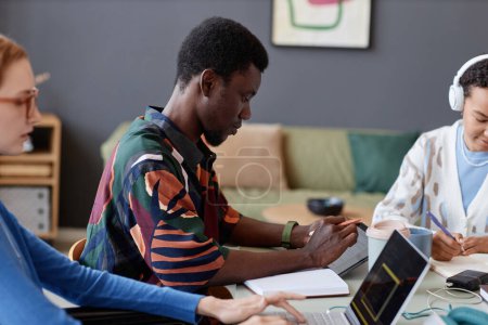 Foto de Retrato de vista lateral del joven negro usando tableta digital mientras trabaja con el equipo en la mesa, espacio para copiar - Imagen libre de derechos