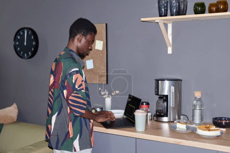 Retrato de vista lateral del joven negro haciendo bebidas en la estación de café en la oficina