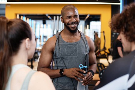 Foto de Retrato de cintura hacia arriba del musculoso hombre negro sonriendo a una pareja joven en una reunión de gimnasia para entrenar con espacio de copia de asistencia - Imagen libre de derechos