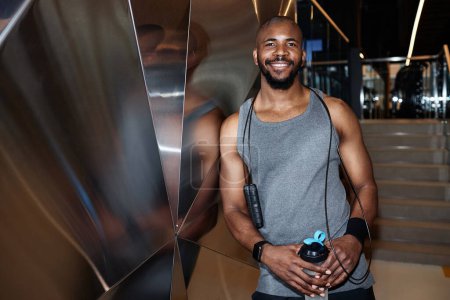 Photo for Waist up portrait of muscular African American man smiling at camera posing in gym interior, shot with flash - Royalty Free Image