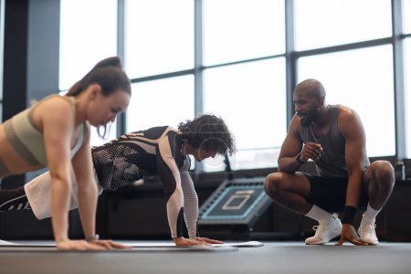 Téléchargez les photos : Portrait latéral de personnes faisant de l'exercice de planche avec l'homme noir comme entraîneur aidant à l'entraînement - en image libre de droit